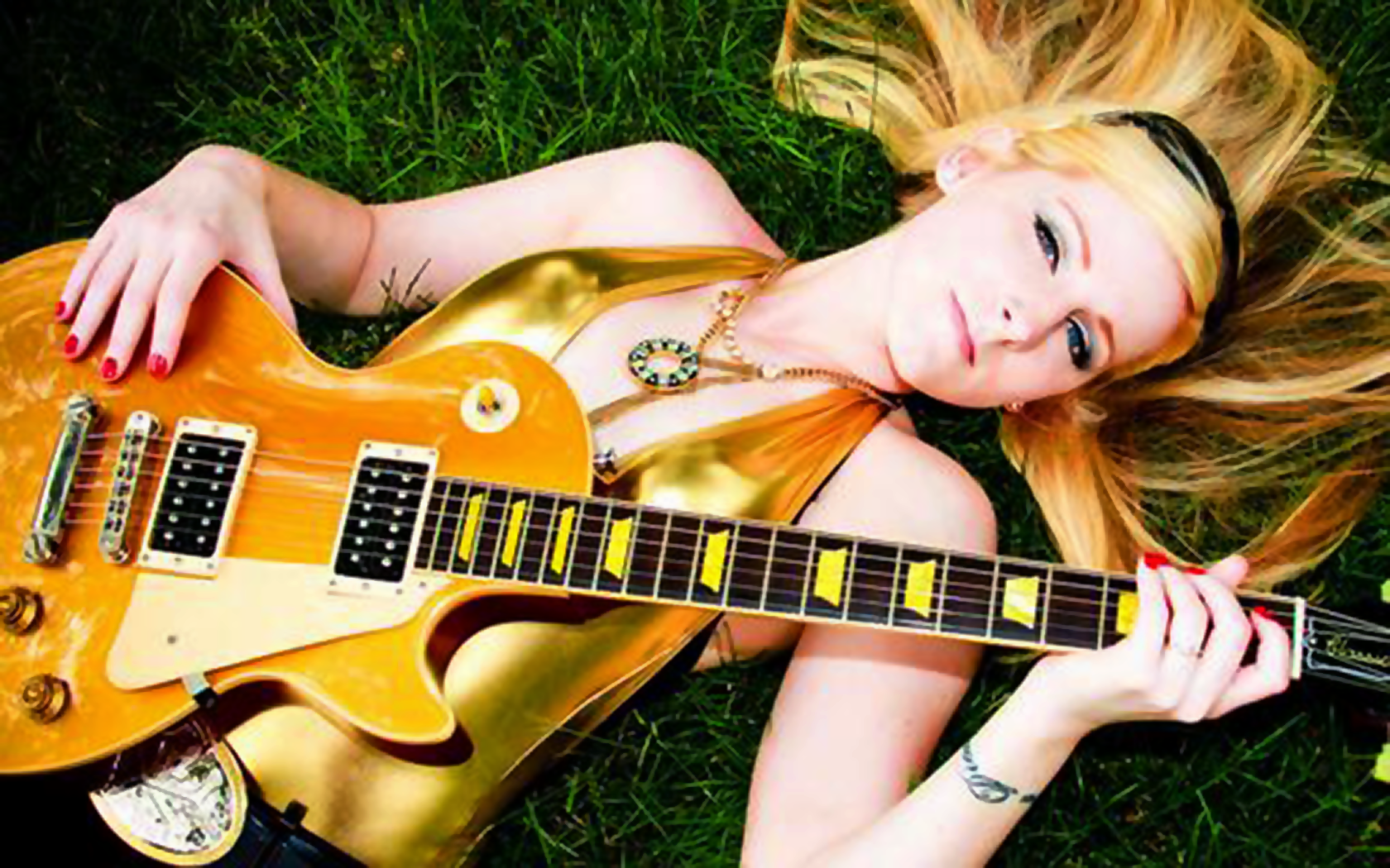 Banksy's Girlfriend, Alexis Smith laying on the grass with an electric guitar across her body and her blonde hair flowing outward.